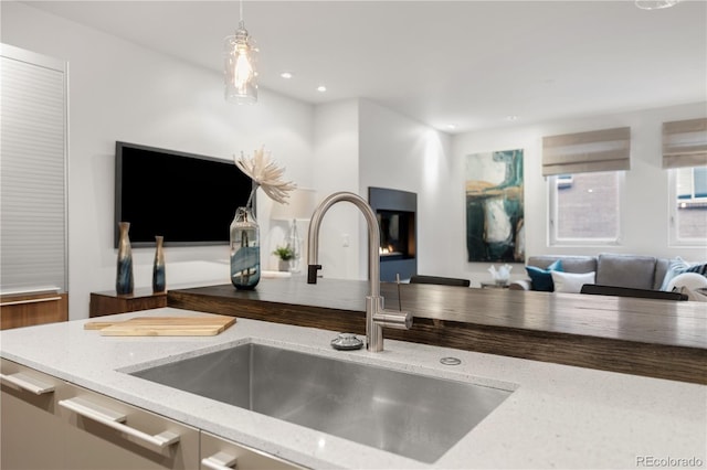 kitchen featuring open floor plan, light stone counters, recessed lighting, hanging light fixtures, and a sink