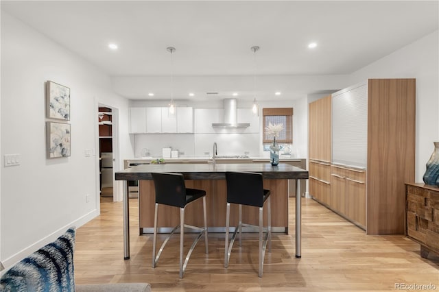 kitchen with modern cabinets, wall chimney range hood, a breakfast bar area, light wood-style flooring, and white cabinetry