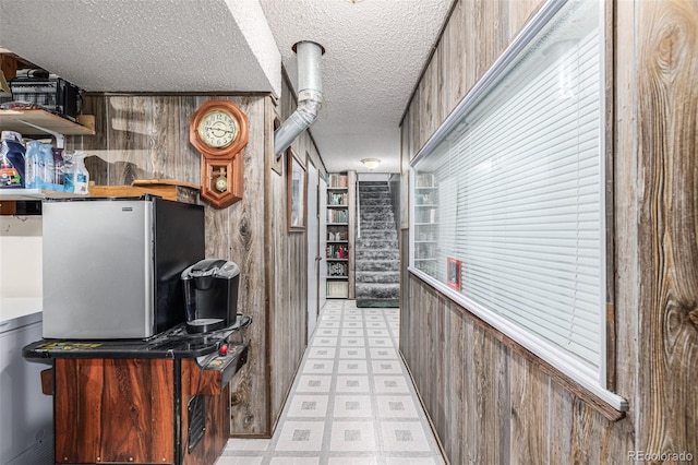 kitchen featuring a textured ceiling, stainless steel fridge, and wood walls