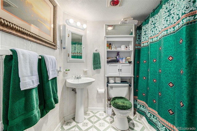 bathroom featuring a textured ceiling, toilet, and tile walls