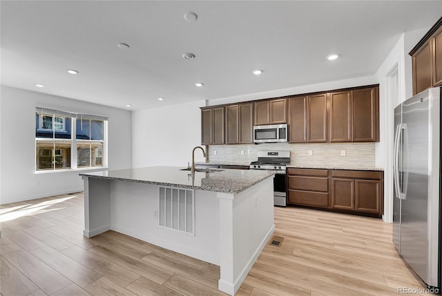 kitchen with light wood-style flooring, a center island with sink, stainless steel appliances, and a sink