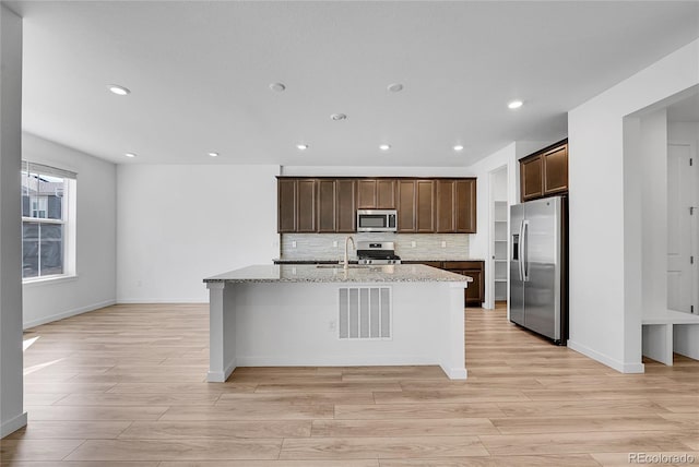 kitchen with dark brown cabinetry, a center island with sink, appliances with stainless steel finishes, and backsplash