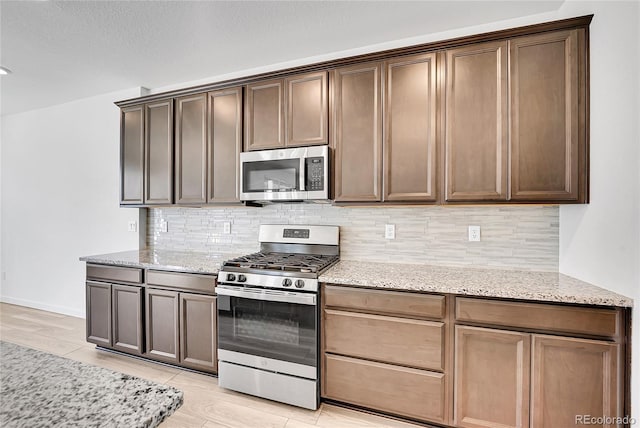 kitchen featuring light stone countertops, tasteful backsplash, stainless steel appliances, and light wood-style flooring