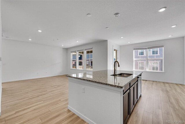 kitchen with light stone counters, a sink, light wood-type flooring, dishwasher, and an island with sink