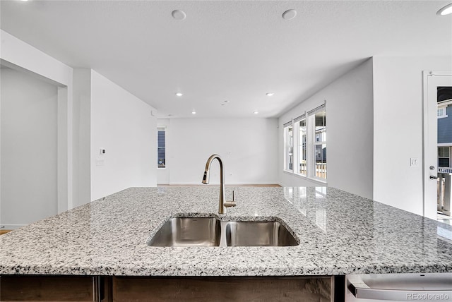 kitchen with light stone counters, recessed lighting, open floor plan, a sink, and an island with sink