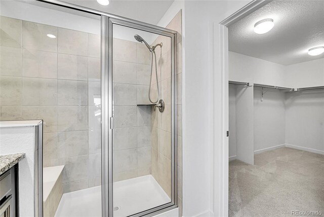 bathroom with a walk in closet, a shower stall, a textured ceiling, and vanity