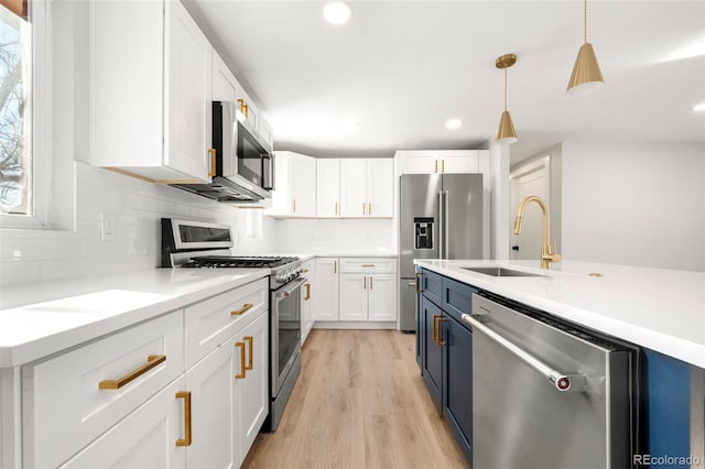 kitchen with appliances with stainless steel finishes, blue cabinetry, light hardwood / wood-style flooring, white cabinets, and hanging light fixtures