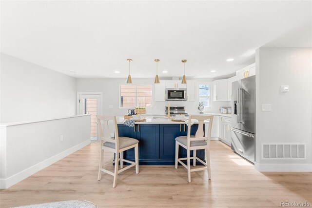 kitchen featuring appliances with stainless steel finishes, an island with sink, a breakfast bar area, white cabinets, and hanging light fixtures