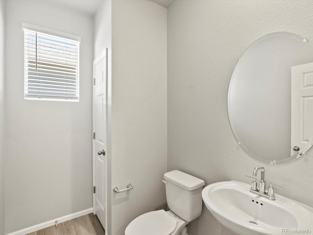 half bath with toilet, baseboards, a sink, and wood finished floors