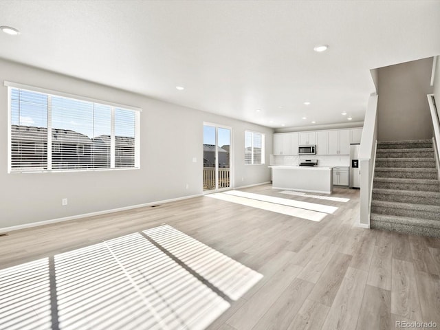 unfurnished living room with light wood-type flooring, stairway, baseboards, and recessed lighting