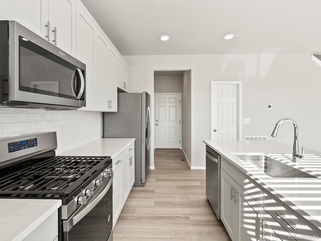 kitchen with light wood-style flooring, a sink, light countertops, appliances with stainless steel finishes, and decorative backsplash