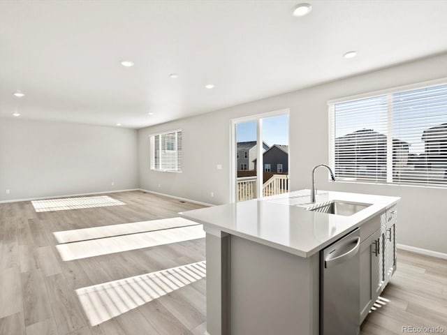 kitchen featuring light wood finished floors, light countertops, stainless steel dishwasher, and a sink