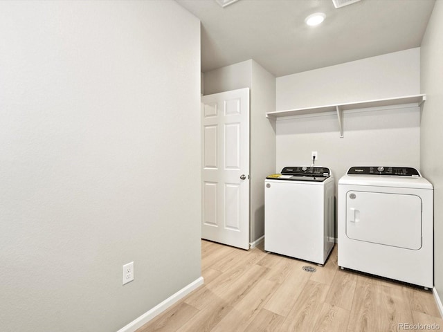 clothes washing area featuring laundry area, baseboards, light wood finished floors, and washing machine and clothes dryer