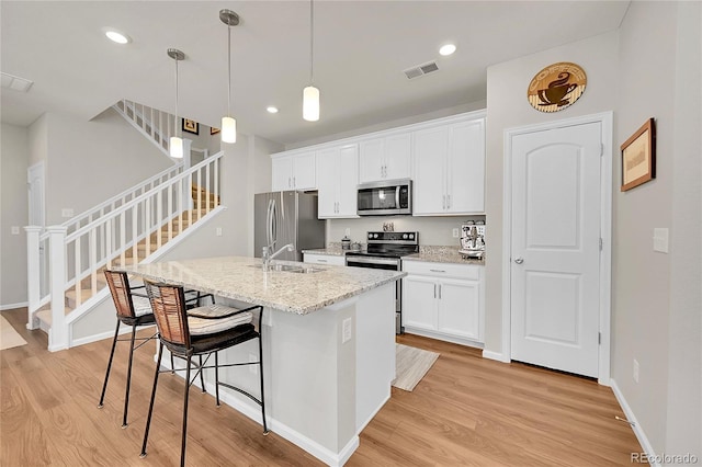 kitchen with pendant lighting, appliances with stainless steel finishes, a kitchen island with sink, white cabinetry, and light hardwood / wood-style floors