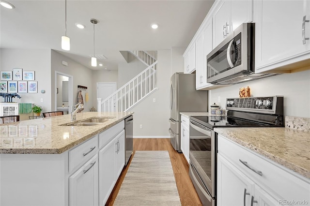 kitchen featuring appliances with stainless steel finishes, pendant lighting, sink, white cabinets, and a center island with sink