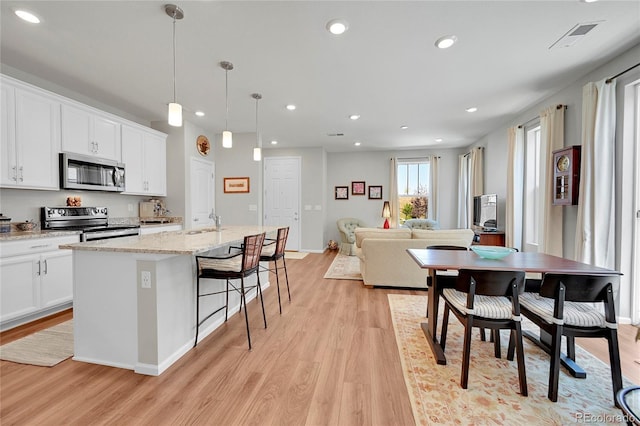 kitchen with white cabinetry, appliances with stainless steel finishes, pendant lighting, and an island with sink