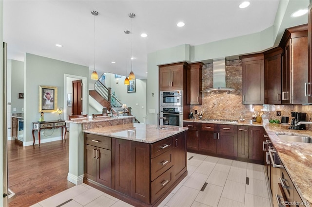 1344 S Saint Paul St, Denver, CO 80210 - kitchen featuring wall chimney exhaust hood, a kitchen island with sink, appliances with stainless steel finishes, decorative light fixtures, and tasteful backsplash