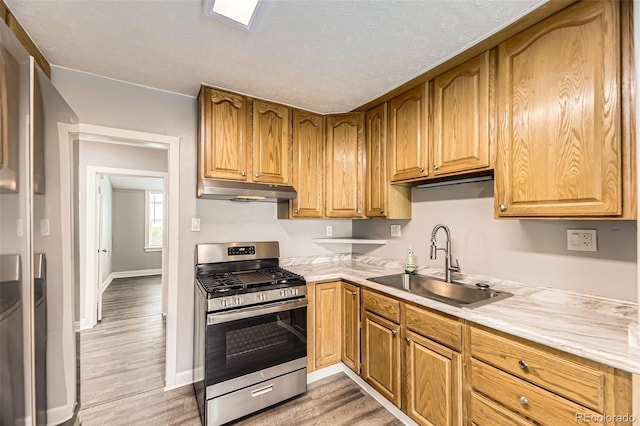 1187 Syracuse St, Denver, CO 80220 - kitchen featuring stainless steel gas stove, under cabinet range hood, light wood finished floors, light countertops, and brown cabinets