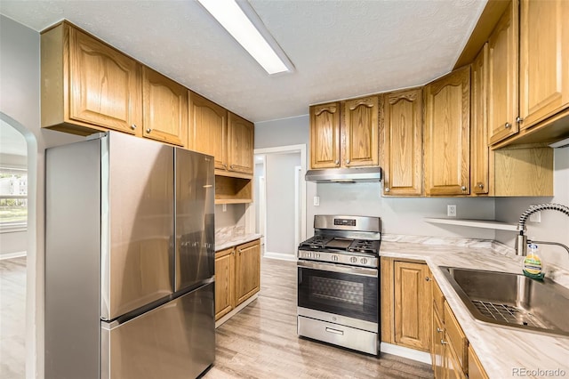 1187 Syracuse St, Denver, CO 80220 - kitchen featuring appliances with stainless steel finishes, under cabinet range hood, light countertops, light wood-style floors, and arched walkways