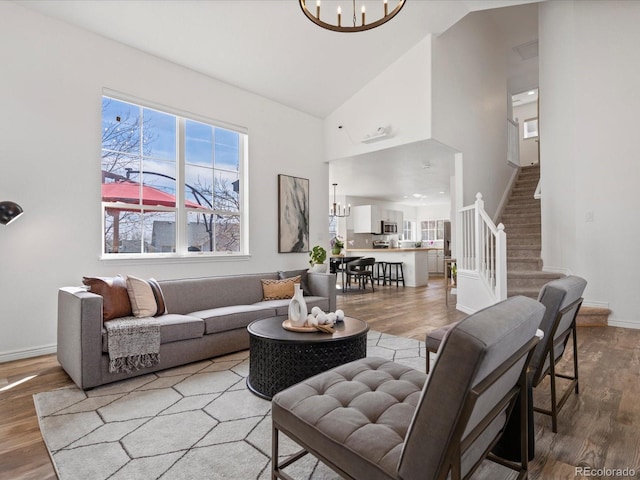 living area with stairway, wood finished floors, baseboards, high vaulted ceiling, and a notable chandelier