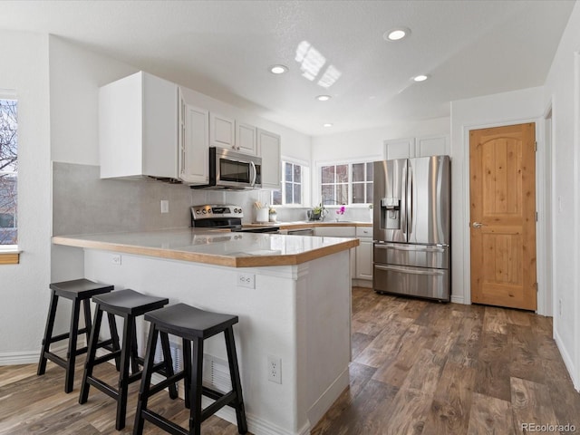 kitchen featuring appliances with stainless steel finishes, a peninsula, dark wood-style flooring, and light countertops