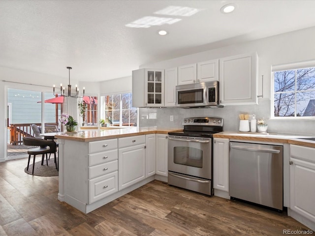 kitchen featuring glass insert cabinets, appliances with stainless steel finishes, a peninsula, dark wood-style floors, and white cabinets