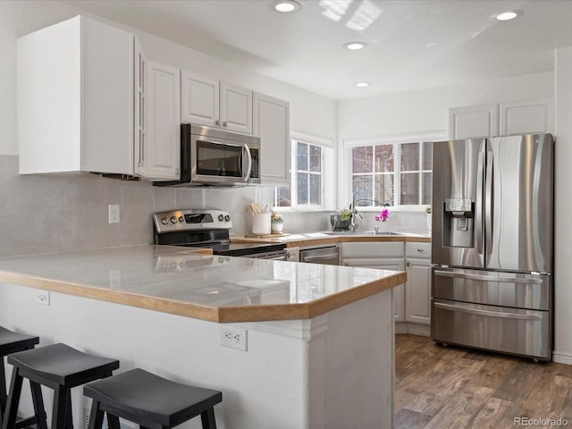 kitchen featuring a sink, a kitchen breakfast bar, light wood-style floors, appliances with stainless steel finishes, and a peninsula