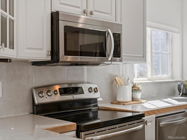 kitchen featuring stainless steel appliances, white cabinets, decorative backsplash, and light countertops