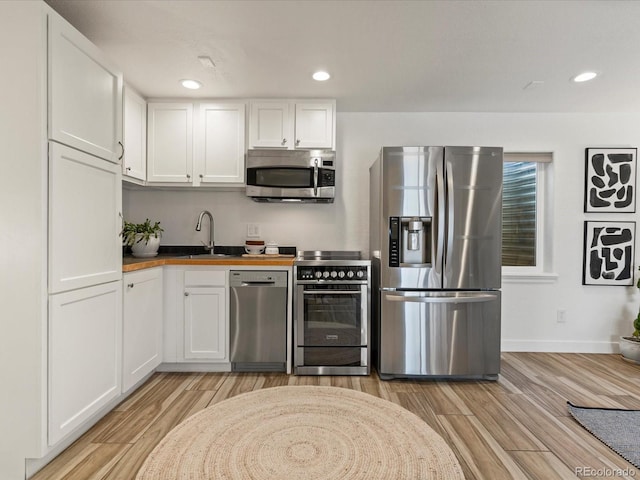 kitchen with a sink, stainless steel appliances, light wood-style floors, and white cabinetry