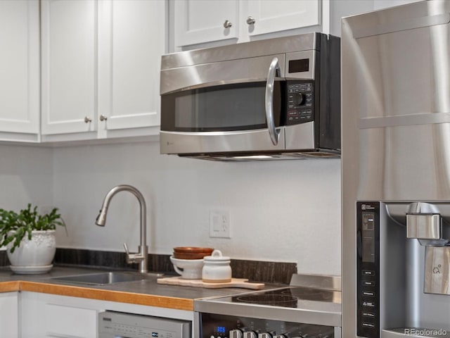 kitchen featuring a sink, stainless steel microwave, dishwashing machine, and white cabinetry