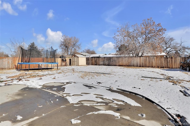 snowy yard featuring a storage shed and a trampoline