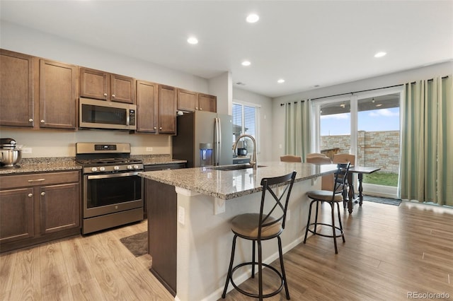 16369 Alberta Dr, Parker, CO 80134 - kitchen featuring stainless steel appliances, a sink, a kitchen breakfast bar, light wood-style flooring, and light stone counters