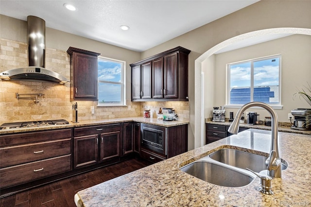 kitchen featuring wall chimney exhaust hood, a sink, stainless steel appliances, light stone counters, and dark wood-type flooring