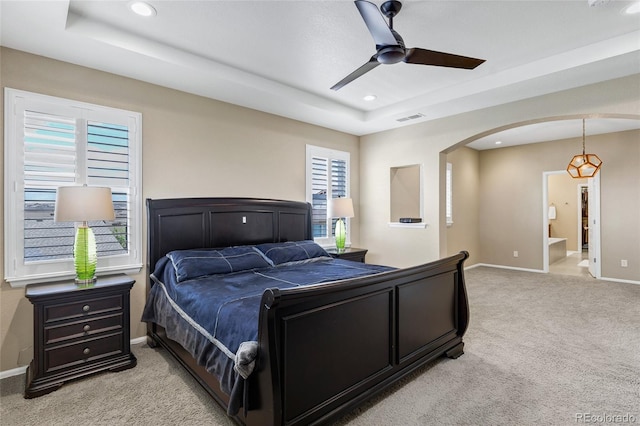bedroom with arched walkways, light colored carpet, baseboards, a raised ceiling, and recessed lighting