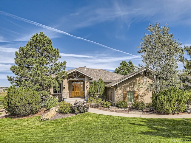 view of front of property featuring a shingled roof, a front lawn, stone siding, and stucco siding