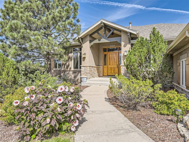 doorway to property featuring stone siding, stucco siding, and roof with shingles