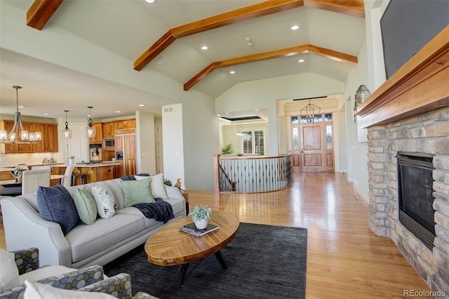 living room featuring beamed ceiling, a chandelier, a fireplace, and light wood finished floors