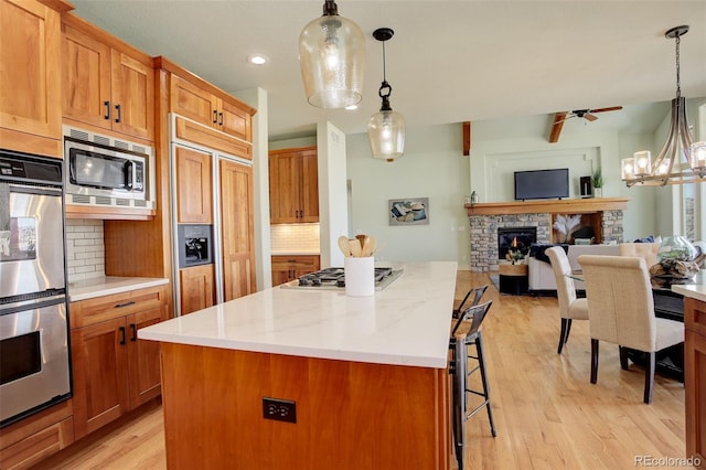 kitchen featuring tasteful backsplash, built in appliances, open floor plan, a breakfast bar, and a stone fireplace