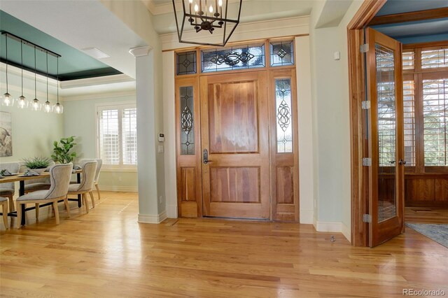 entryway featuring baseboards, a chandelier, crown molding, and light wood finished floors