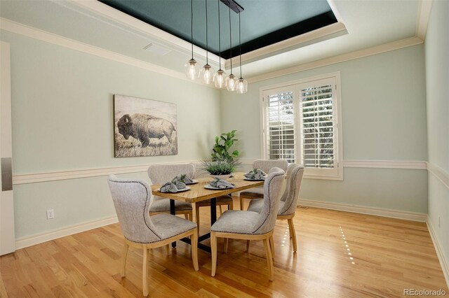 dining space with baseboards, a raised ceiling, wood finished floors, and crown molding