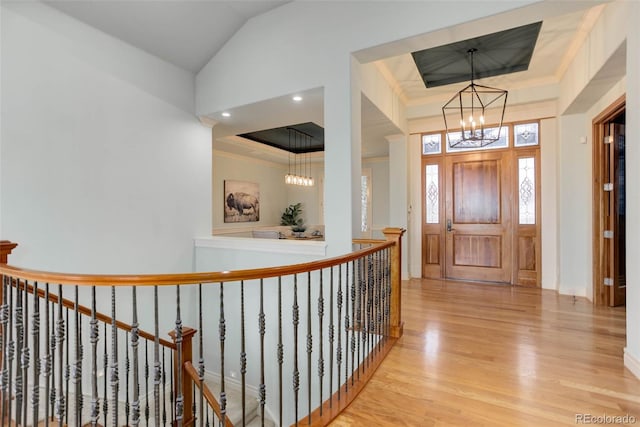 entryway featuring a tray ceiling, a notable chandelier, wood finished floors, and crown molding