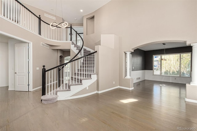 stairway with decorative columns, a chandelier, wood-type flooring, and a high ceiling