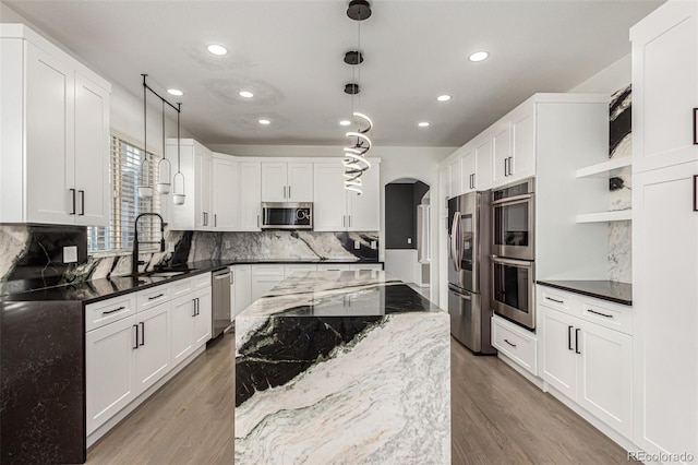 kitchen with dark stone counters, hanging light fixtures, light hardwood / wood-style floors, white cabinetry, and stainless steel appliances