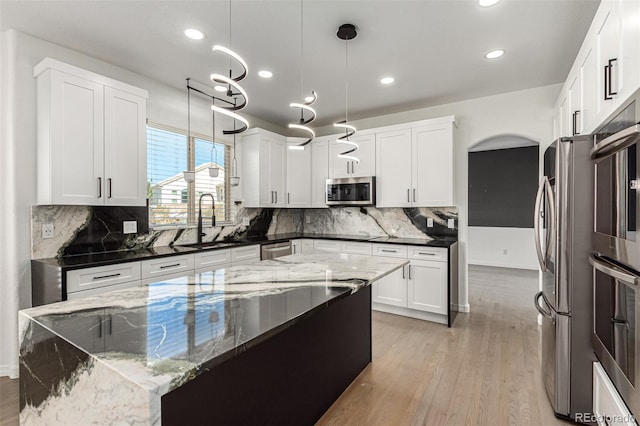 kitchen with white cabinetry, sink, dark stone counters, decorative light fixtures, and appliances with stainless steel finishes