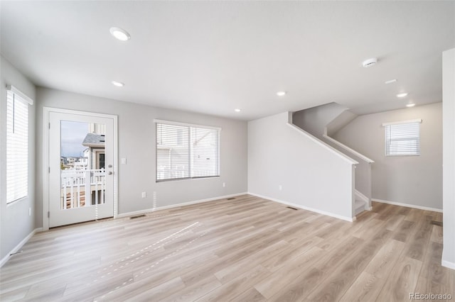 unfurnished living room featuring plenty of natural light, stairs, light wood-type flooring, and recessed lighting