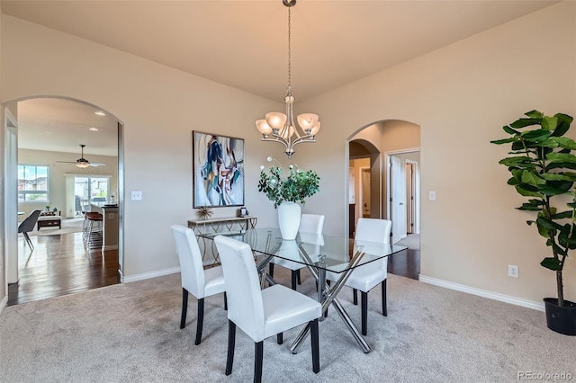 carpeted dining space with baseboards, arched walkways, and ceiling fan with notable chandelier