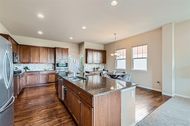 kitchen with a sink, dark stone counters, stainless steel appliances, decorative backsplash, and dark wood-style floors
