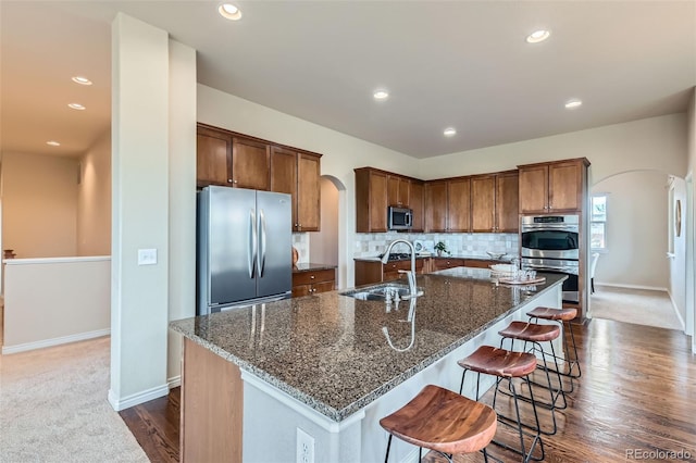 kitchen featuring a kitchen breakfast bar, arched walkways, appliances with stainless steel finishes, a sink, and an island with sink