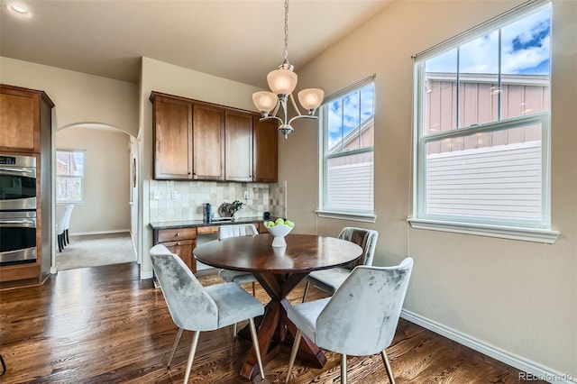 dining room with dark wood-style flooring, a notable chandelier, arched walkways, plenty of natural light, and baseboards