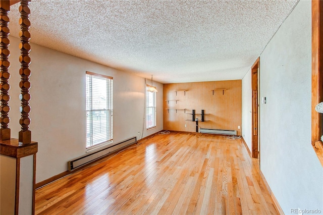 unfurnished room featuring a baseboard radiator, light wood-style flooring, a textured ceiling, and wooden walls